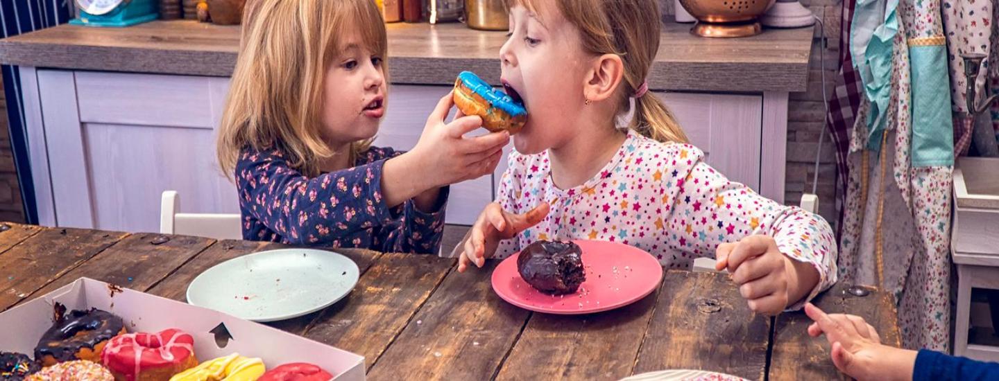 Two girls eating donuts together in the kitchen.
