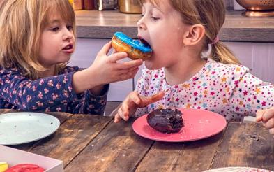 Two girls eating donuts together in the kitchen.