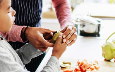 An adult helping a child to prepare fruit and vegatables