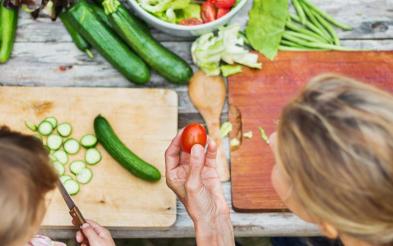 A woman teching a child to prepare vegetables.