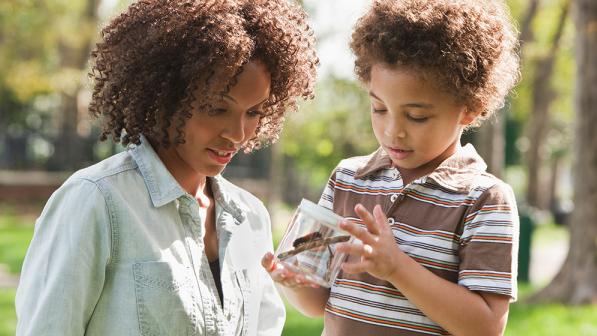 A mother playing outdoors with her child with a cardboard box.