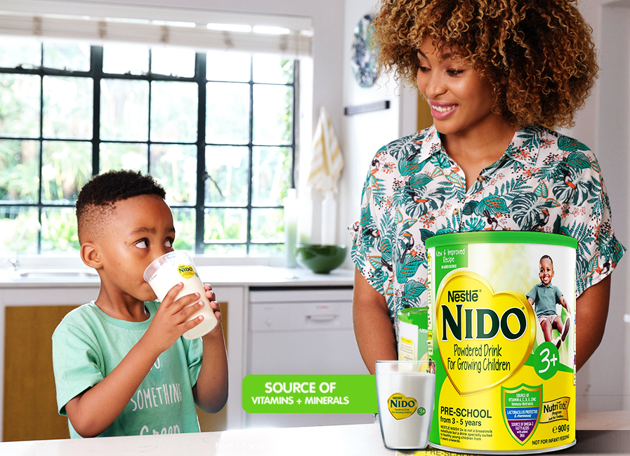 A boy drinking Nido 3 plus with a woman by his side inside the kitchen.